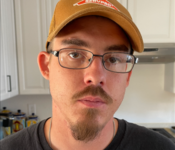 Male employee with mustache and goatee wearing glasses and a SERVPRO logo'd hat