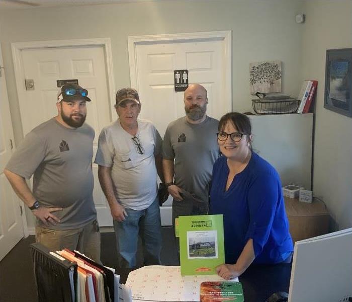 Woman and three men standing behind desk. Woman holding SERVPRO ERP