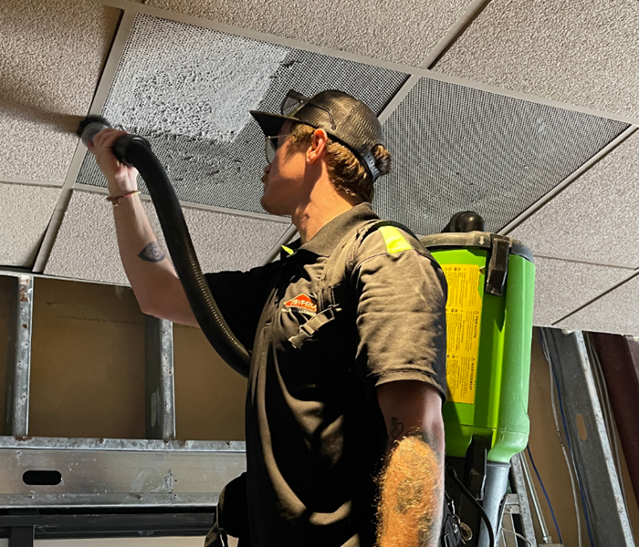 Male employee in SERVPRO uniform HEPA vacuuming an air vent.